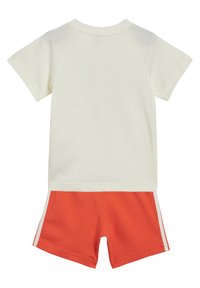 Maglietta a maniche corte crema con maniche raglan abbinata a pantaloni corti arancioni con dettagli a strisce laterali. Realizzata in morbido tessuto di cotone.