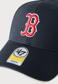 Καπέλο σε ναυτικό μπλε χρώμα, κατασκευασμένο από ύφασμα, με κεντητό κόκκινο λογ ότυπο "B" στο εμπρόσθιο μέρος, διαθέτει κυρτό γείσο και κίτρινη και μαύρη ετικέτα με την ένδειξη "47 YOUTH".