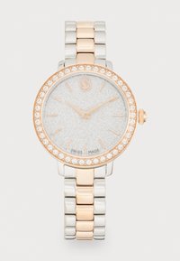 Montre-bracelet en argent et or rose avec un cadran argenté scintillant, une lunette ornée de cristaux et un bracelet en métal à maillons alternés.
