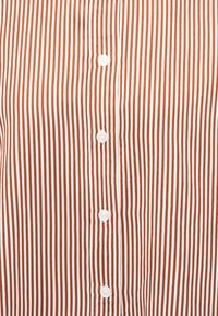 Κοντινή λήψη μιας κάθετα ριγέ πουκαμισο σε χρώμα σκουριάς και λευκό με κεντρικό καβάλο κουμπιών με λευκά κουμπιά.