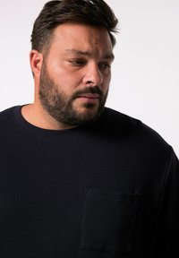 Tummansininen vohvelikuvioinen pitkähihainen paita, jossa on pyöreä kaula-aukko ja neliömäinen läpiväritys vasemmassa rinnassa.