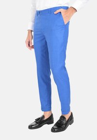 Pantaloni blu su misura con una texture liscia, vestibilità slim e tasche laterali, abbinati a mocassini neri con un pon-pon decorativo.