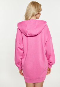 Abito felpa over-size rosa con una grande cappuccio, polsini a coste e una trama liscia; presenta spalle scese e una vestibilità morbida.