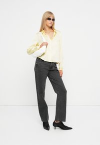 Żółta koszula z długim rękawem, zestawiona z luźnymi czarnymi dżinsami i czarnymi butami na obcasie. Biała torebka i okulary przeciwsłoneczne dopełniają stylizację.