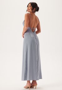 Lång, ärmlös klänning i ljusblå satin med låg rygg, justerbara banddetaljer och en svävande silhuett, kompletterad med nude klackar.