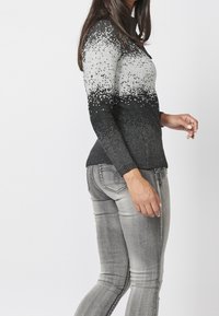 Pull en tricot dégradé de nuances de gris et de noir, avec un motif texturé, une coupe ajustée et des poignets côtelés, associé à un jean gris.