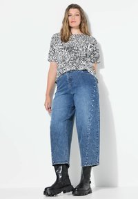 Černobílá paisley košile s krátkým rukávem kombinovaná s modrými džínovými širokými kalhotami s vysokým pasem, které mají cvočkové detaily a černé kotníkové boty.