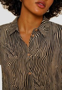 Bruine en zwarte gestreepte overhemd met kraag, gemaakt van een gemêleerd stof en met houten knopen. De details omvatten golvende patronen.