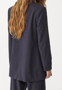 Merijanssinauha bleiseri, jossa on pitkät hihat, yksittäinen napitus ja muotoiltu siluetti. Valmistettu sileästä kankaasta, jossa on matta pinta.