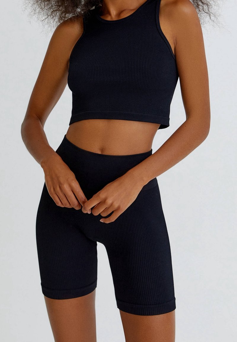 Conjunto de top corto de canalé negro y pantalones cortos de cintura alta. La tela tiene un acabado texturizado, con un diseño ajustado y un aspecto sin costuras en los bordes.
