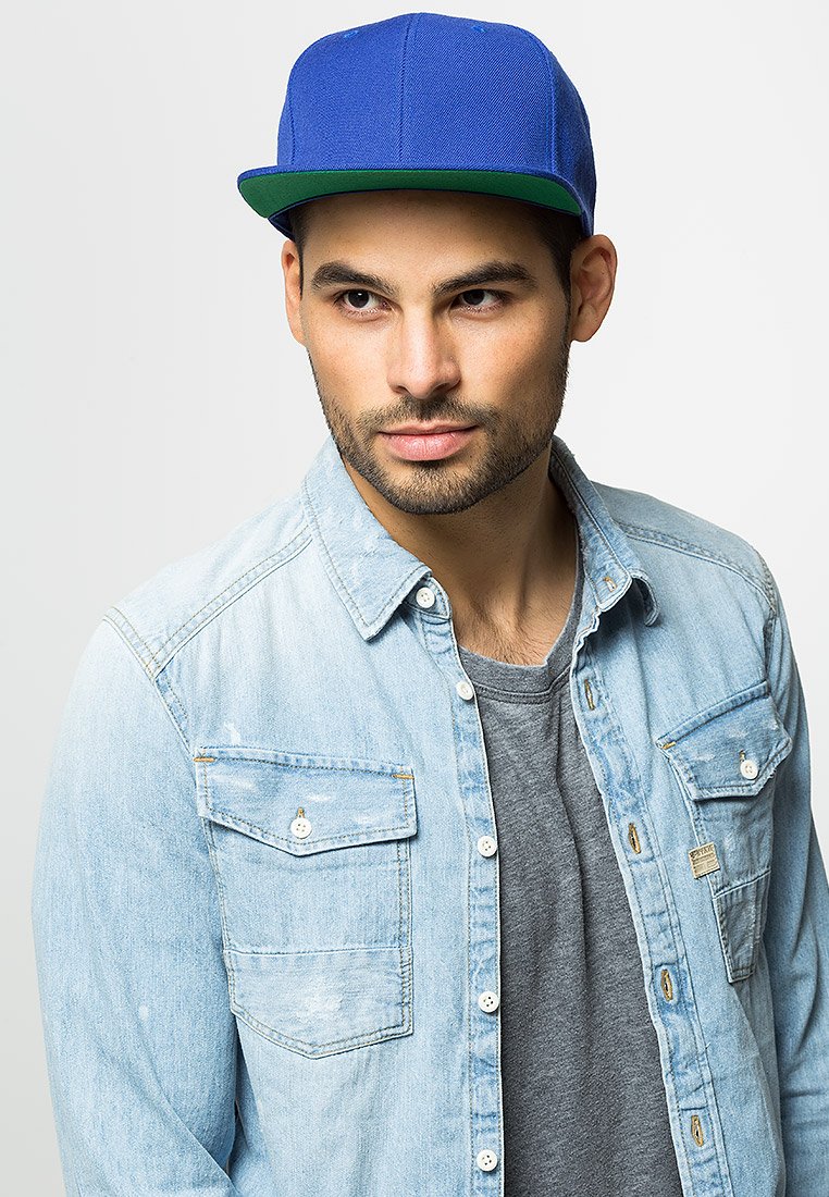 Blå baseballcaps med flat brem, brukt sammen med en lys denimskjorte over en grå T-skjorte. Skjorten har knappebelagte brystlommer.