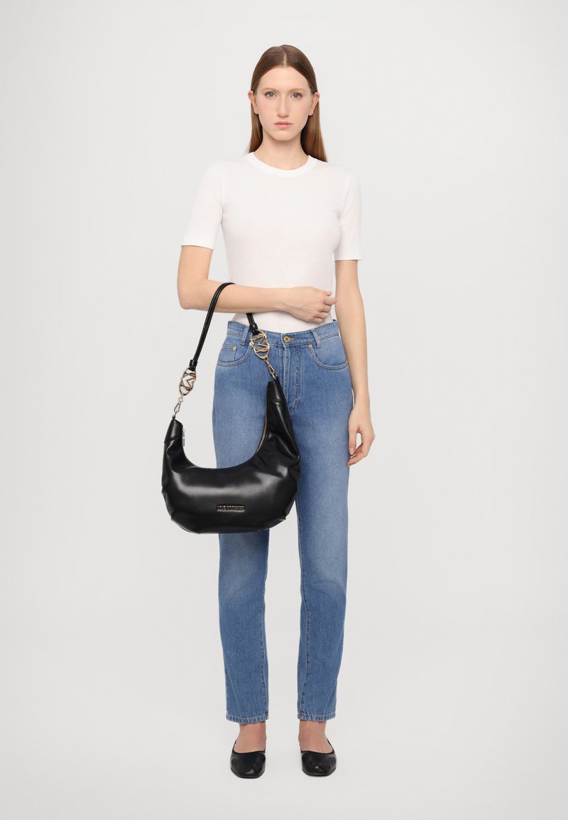 Saco hobo de couro preto com uma forma estruturada, alça curta e detalhes em tom de ouro. Textura suave com um emblema da marca na frente.