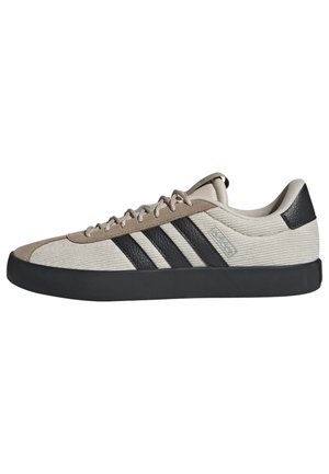 Zapatillas de lona beige con rayas negras, acentos grises, puntera redonda, suela plana de goma, parte superior texturizada y diseño con cordones.