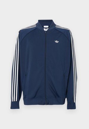 Laivastonsininen vetoketjullinen verkkatakki polyesteriä, jossa valkoiset kolmisuora raidat hihoissa ja pieni valkoinen logo rinnassa.