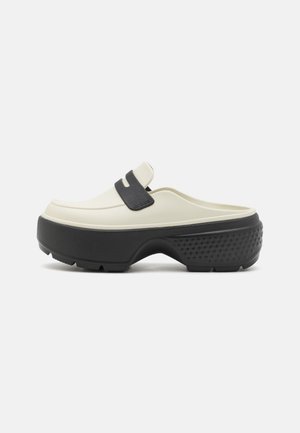 Chaussure à enfiler avec une semelle plateforme noire épaisse et une tige crème ornée d'une lanière noire sur le coup de pied.