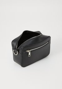 Trousse de maquillage rectangulaire noire en cuir texturé. Elle possède une fermeture éclair en argent, une poignée intégrée et une poche zippée à l'avant.