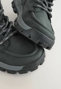 Bottes de randonnée noires en cuir lisse, avec des accents texturés gris, des semelles robustes et des lacets tressés pour un maintien sûr.