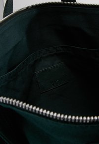 Musta kangaskassi, jonka sisällä on sileä tekstuuri, hopeinen vetoketju ja pieni musta nahkaleima sivussa.