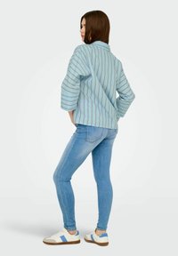 Camicia oversized a righe blu chiaro con maniche a tre quarti, abbinata a jeans blu chiaro aderenti e scarpe da ginnastica bianche con strisce blu.