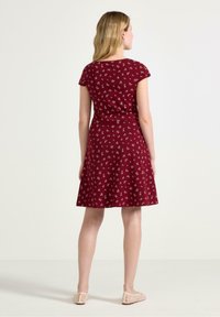Bordeaux kjole med en flagrende nederdel, korte ærmer og små blomster. Lavet af blødt stof, har en figursyet talje. Uformelt design.