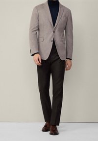 Blazer texturé gris avec des revers en pointe sur un col roulé noir, associé à un pantalon marron foncé et des mocassins bruns.