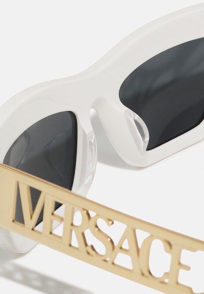 Valged üliüllatavad päikeseprillid tumedate läätsedega. Omavad silmapaistvat kuldset visiiri, millel on graveeritud suurtähtedega "VERSACE". Sujuv tekstuur, voolujooneline disain.