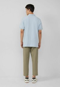 Helles blaues Poloshirt mit kurzen Ärmeln aus Baumwolle. Kombiniert mit hellolivgrünen Hosen im lässigen Schnitt und athletischen Schuhen.