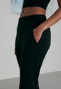 Pantaloni sportivi neri con una texture liscia, vita alta e tasca laterale. Design aderente adatto per l'abbigliamento attivo.
