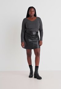 Zwart leren minirok met voornaden, gecombineerd met een fitted grijs longsleeve T-shirt. Model draagt chunky zwarte laarzen. Eenvoudig, textuurontwerp.