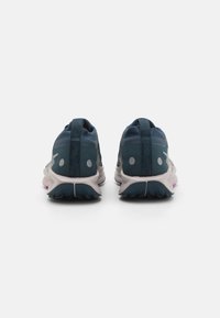 Zapatos deportivos de malla azules con suela gris, que presentan un diseño texturizado, tiradores y acentos circulares blancos en el talón.