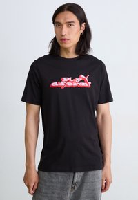 Sort bomulds t-shirt med rød og hvid grafisk tekst "Play different" og et Puma-logo på fronten. Korte ærmer, crew neck-design.