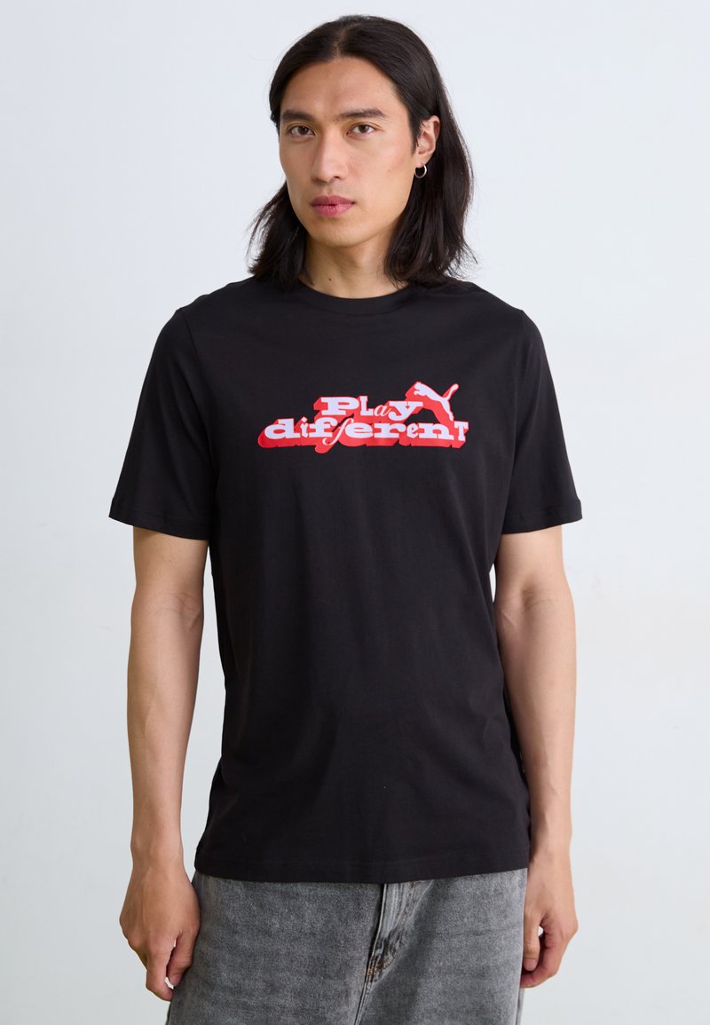 Sort bomulds t-shirt med rød og hvid grafisk tekst "Play different" og et Puma-logo på fronten. Korte ærmer, crew neck-design.