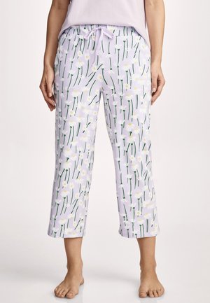 Woman wearing cropped lavender pajama pants with white daisy flower pattern and a white drawstring waistband, barefoot.