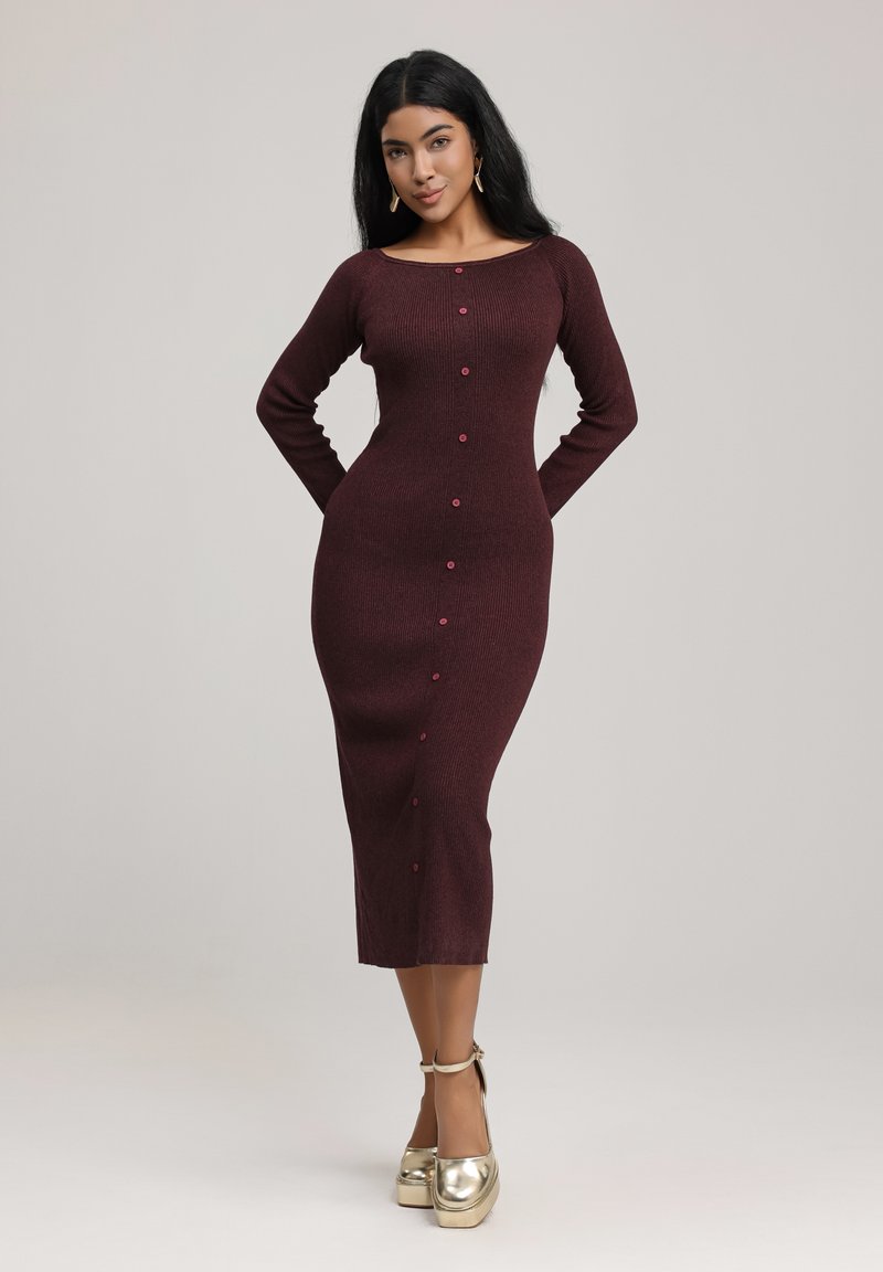Burgundy ribbed neulepuku pitkillä hihoilla ja venepääntiellä. Sisältää napitettava etuosan ja midi-pituuden. Yhdistetty kultaisiin platform-kenkiin.
