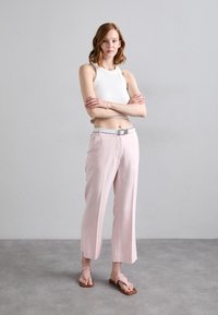 Pantaloni roz deschis cu talie înaltă, cu un croi drept, asortați cu un top din bumbac alb, mulat, și flip-flops roz. O curea argintie a fost adăugată ca accent.