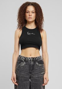 Fekete bordázott crop top magas nyakú kivágással �és fehér jellegzetes grafikával. Magas derekú fekete, megviselt farmernadrággal párosítva.