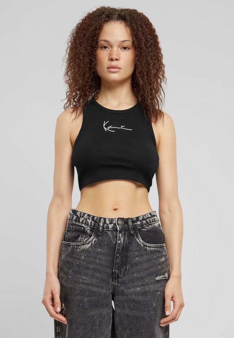 Top corto nero a coste con collo alto e grafica bianca con firma. Abbinato a jeans in denim neri sfilacciati a vita alta.