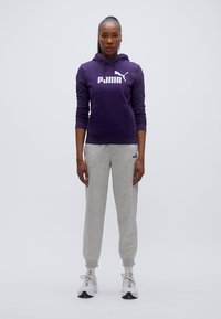 Μωβ φούτερ με κουκούλα και λευκό λογότυπο, συνδυασμένο με ανοιχτό γκρι φόρμα. Το μοντέλο φοράει λευκά αθλητικά παπούτσια με γκρι λεπτομέρειες.