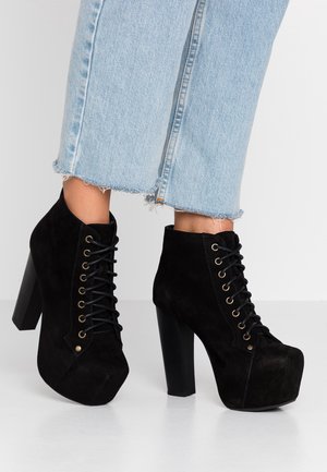 Schwarze Wildleder-Plateau-Schnürstiefel bis zum Knöchel, getragen mit hellblauen, gekürzten Jeans mit ausgefranstem Saum auf weißem Boden.