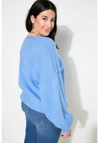 Pull bleu clair surdimensionné avec un tricot doux et texturé, des manches larges et un col festonné, associé à un jean bleu ajusté.