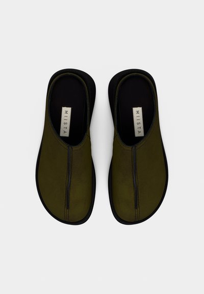 Olívazöld bebújós cipők sima felülettel, fekete talppal és középen végigfutó varrással. Részletezésként márkázott talpbetéttel rendelkeznek.