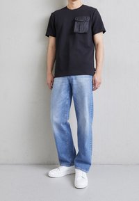 Svart t-shirt med bröstficka, matchad med ljusblå jeans och vita sneakers. Enkel, avslappnad passform med en mjuk textur.