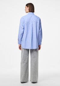 Sininen raidallinen paita, jossa on selkäosa, pitkät hihat ja napilliset kalvosimet, yhdistetty harmaisiin leveälahkeisiin housuihin. Sileä kangas, rento istuvuus.