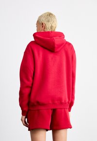 Rød hettegenser med en stor, tettsittende hette, laget av et mykt materiale. Ribbede mansjetter og nederkant, kombinert med matchende røde shorts.
