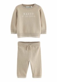 Pull en tricot beige avec le texte "BAKER", manches longues et accents de boutons ; associé à un pantalon beige assorti avec une taille à cordon.