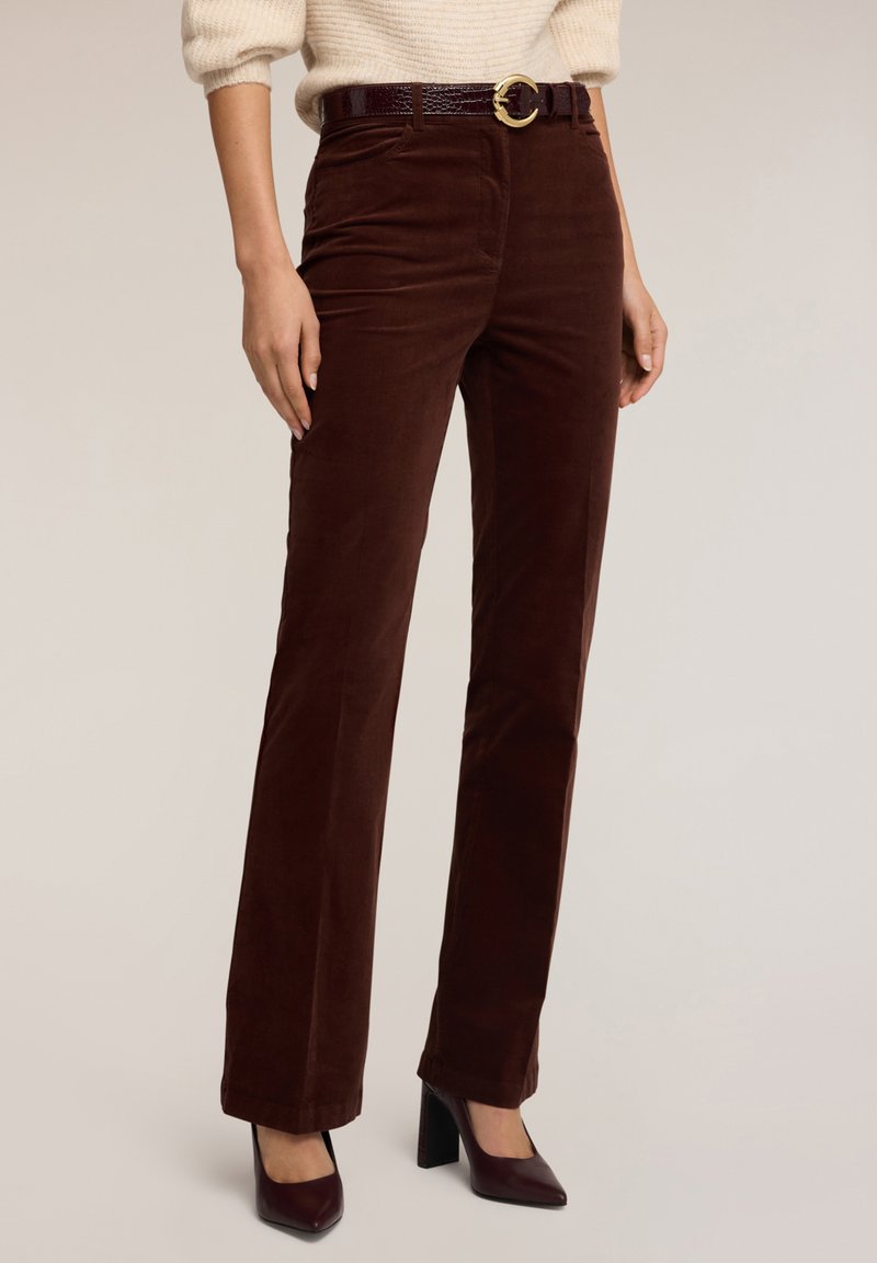 Pantalones de pana marrón con un corte recto, que incluyen un cinturón burdeos brillante y una hebilla circular dorada, combinados con zapatos de tacón.