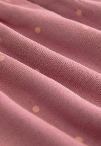 Roze stof met subtiele textuur, voorzien van verhoogde, ronde, lichtoranje stippen. Het materiaal lijkt zacht en licht rekbaar te zijn.