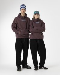 To modeller har på seg oversized, mørk lilla hettegensere med blå logo-detaljer, kombinert med svarte posete bukser. Den ene har på seg en stripete lue, mens den andre har en grønn caps.