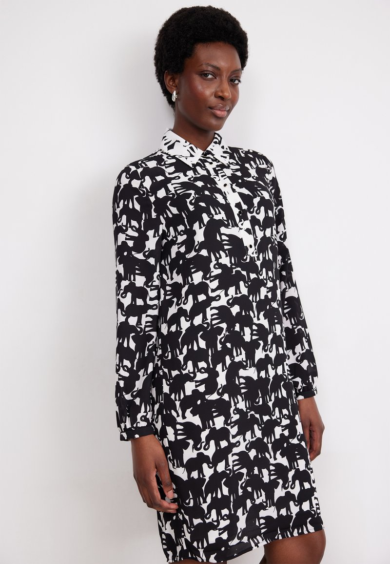 Schwarz-weißes Kleid mit einem durchgehenden Tier-Silhouettenmuster, langen Ärmeln und einem kragenförmigen Halsausschnitt mit Knopfdetails.