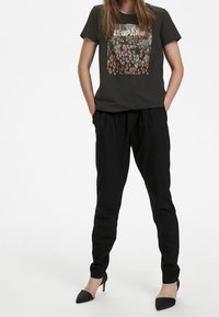 Tmavě šedé tričko s leopardím potiskem a kovovými akcenty, spárováno s černými zúženými kalhotami a černými lodičkami.